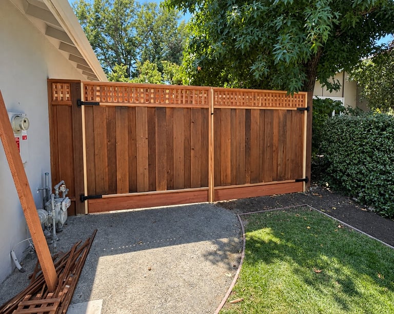 Wooden driveway gate with lattice top and metal trim installed in a residential yard with trees and lawn