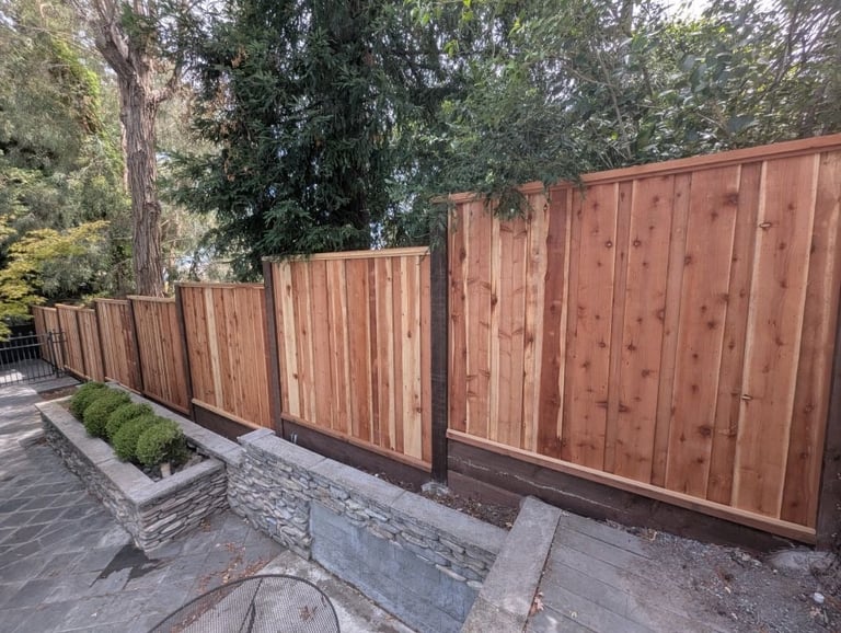 New redwood fence panels installed along a concrete patio with mature trees in the background
